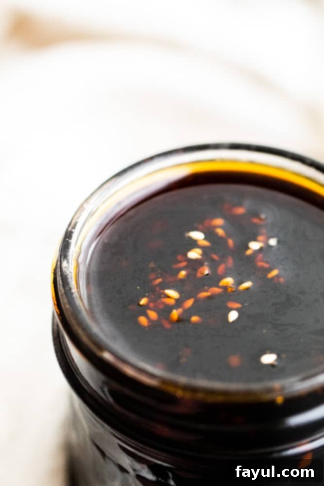 This Easy Homemade Teriyaki Sauce recipe is a great DIY version of this Asian favorite. This sauce pairs perfect with stir fry, chicken, beef and vegetables. This simple Japanese sauce is ready in about 20 minutes and has the classic teriyaki sauce flavor that we all know and love. #TeriyakiSauce #recipe #Asian Close-up view of homemade teriyaki sauce in a glass mason jar, showcasing its rich, glistening texture, against a blurred white background.