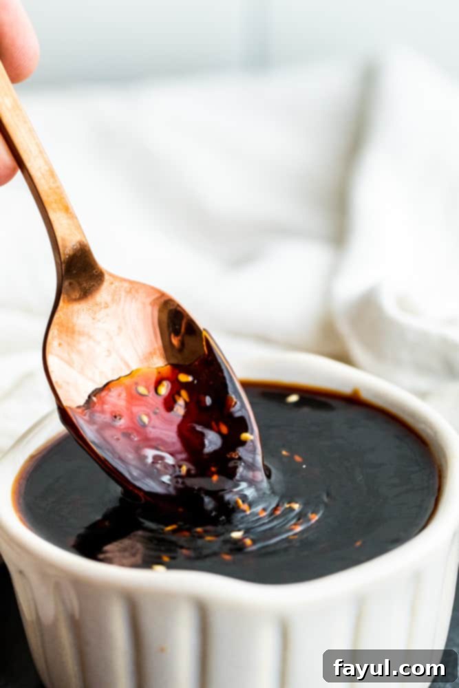 This Easy Homemade Teriyaki Sauce recipe is a great DIY version of this Asian favorite. This sauce pairs perfect with stir fry, chicken, beef and vegetables. This simple Japanese sauce is ready in about 20 minutes and has the classic teriyaki sauce flavor that we all know and love. #TeriyakiSauce #recipe #Asian A gold spoon elegantly dipping into a white bowl filled with glossy homemade teriyaki sauce, illustrating its rich texture and readiness for serving.