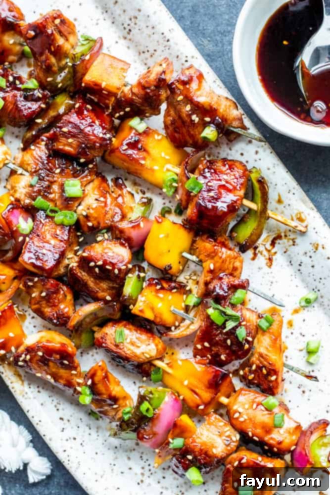 The best Grilled Chicken Teriyaki Kabobs recipe for summer grilling and BBQ. These Japanese-style chicken and mango skewers are tossed in homemade teriyaki sauce, paired with green pepper and red onion. A fantastic recipe for family dinners or healthy meal prep lunches. #dinner #kabobs #BBQ #teriyakichicken Overhead shot of vibrant grilled chicken teriyaki skewers arranged on a white platter, accompanied by a small bowl of savory teriyaki sauce on the side.