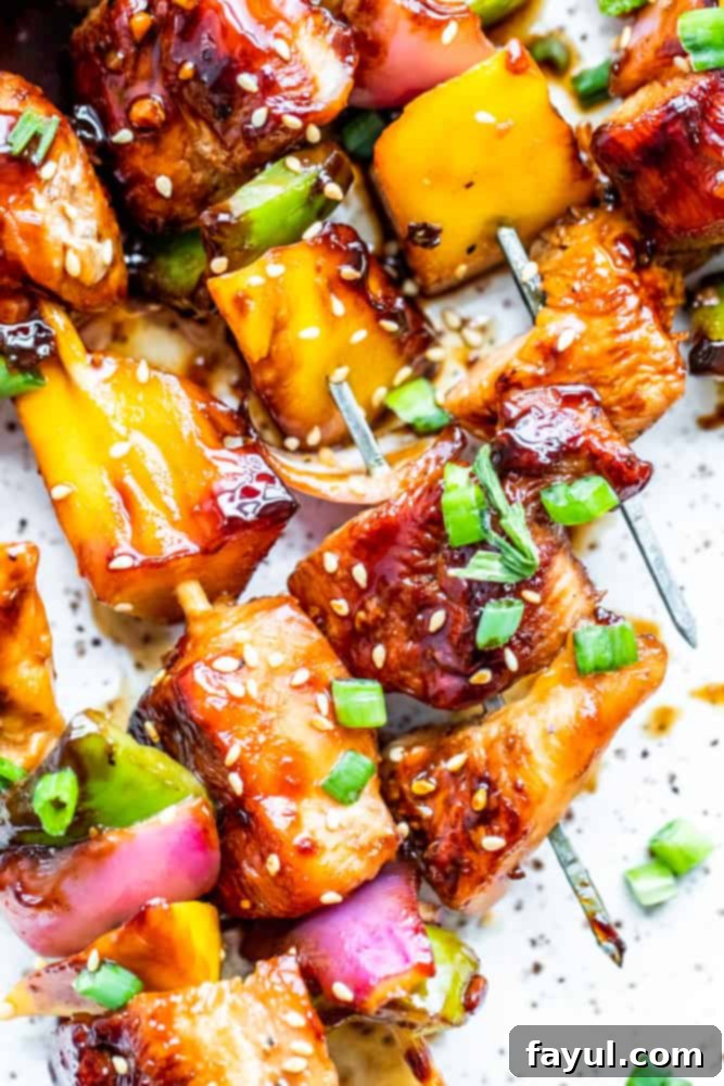 This Grilled Chicken Teriyaki Kabobs recipe is the best for summer grilling and BBQ. These Japanese style skewers are tossed in homemade teriyaki sauce and paired with mango, green pepper and red onion. This recipe is great for family dinners or meal prep for work week lunches. #dinner #kabobs #BBQ Close up shot of perfectly grilled chicken kabobs glistening with teriyaki sauce on a clean white platter.