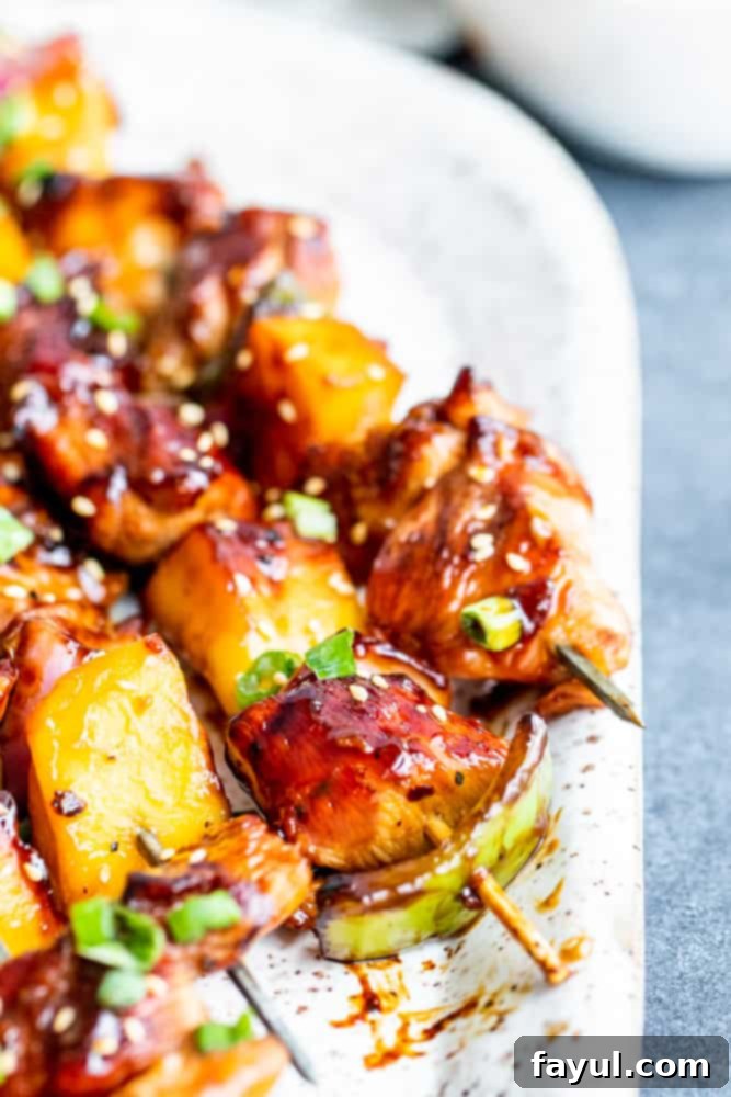 This Grilled Chicken Teriyaki Kabobs recipe is the best for summer grilling and BBQ. These Japanese style skewers are tossed in homemade teriyaki sauce and paired with mango, green pepper and red onion. This recipe is great for family dinners or meal prep for work week lunches. #dinner #kabobs #BBQ Close up shot of golden-brown grilled teriyaki chicken kabobs arranged on a white tray, resting on a blue counter.