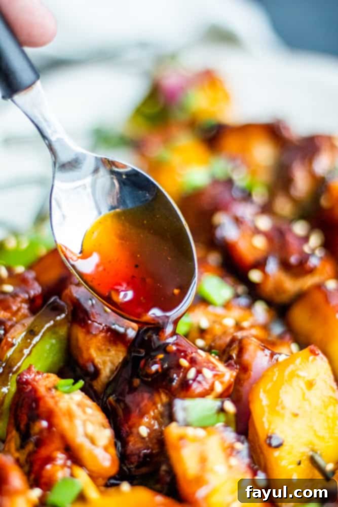 This Grilled Chicken Teriyaki Kabobs recipe is the best for summer grilling and BBQ. These Japanese style skewers are tossed in homemade teriyaki sauce and paired with mango, green pepper and red onion. This recipe is great for family dinners or meal prep for work week lunches. #dinner #kabobs #BBQ Silver spoon gracefully drizzling rich teriyaki sauce over freshly cooked chicken and colorful vegetables.