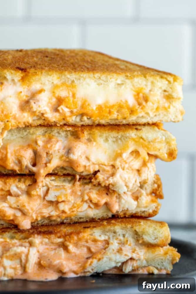 Four golden-brown Buffalo chicken grilled cheese sandwiches stacked high on a black plate, showcasing the crispy bread and hinting at the spicy, cheesy filling within.