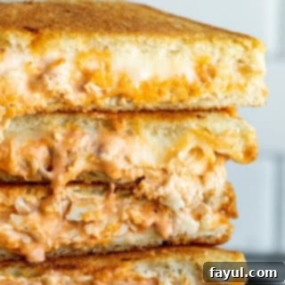 Stack of golden-brown grilled cheese sandwiches on a black plate, with buffalo chicken filling visible.