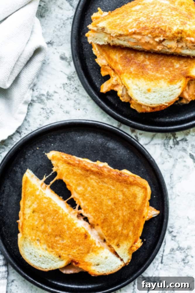 An overhead shot of a perfectly cooked buffalo chicken grilled cheese sandwich on a sleek black plate, artfully placed on a white kitchen counter, ready to be enjoyed.