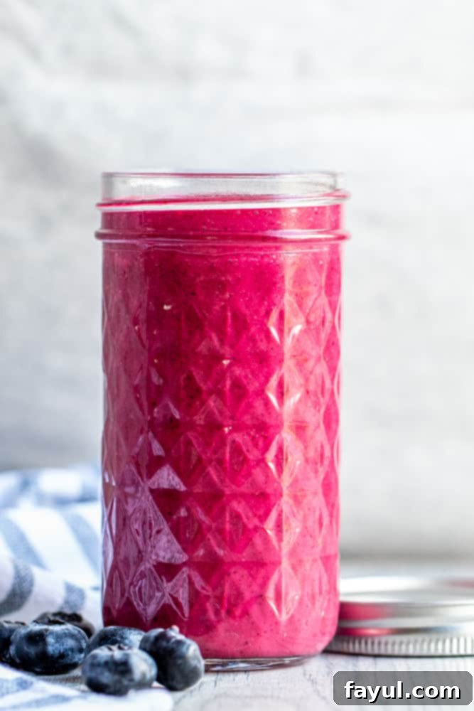 Straight on shot of blueberry vinaigrette in a mason jar on a white counter, with a rustic tea towel beside it. 