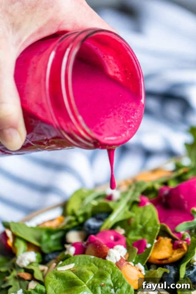 Hand pouring blueberry dressing over a fresh, colorful salad with a mix of greens and fruit.