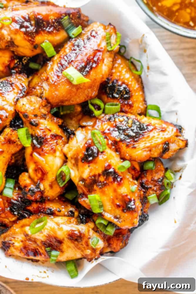 Overhead shot of perfectly grilled BBQ Peach Chicken Wings in a white bowl, with a side of luscious peach sauce, ready to be served. Ideal for summer entertaining and family meals.