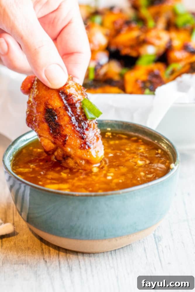 Hand dipping a grilled chicken wing into a small blue bowl of peach sauce on a white kitchen counter, highlighting the delicious interaction.