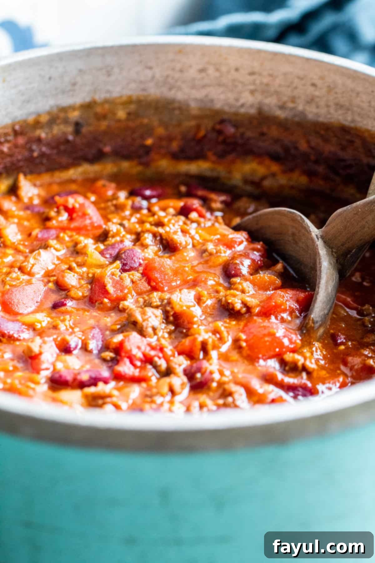 Blue pot filled with chili with a wooden spoon sitting in it, ready to serve.