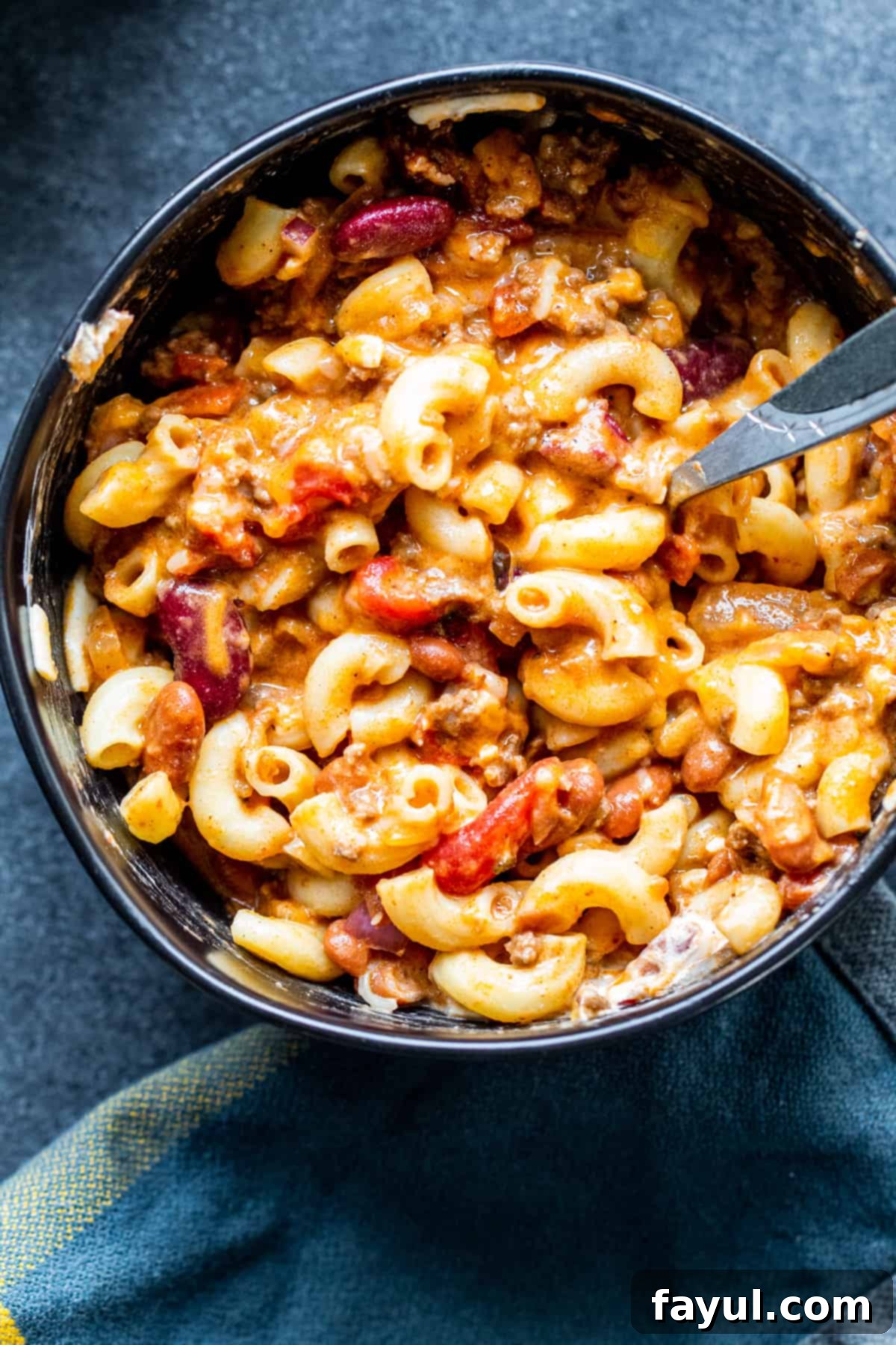 Overhead shot of chili and noodles in black bowl mixed with cheese and sour cream.