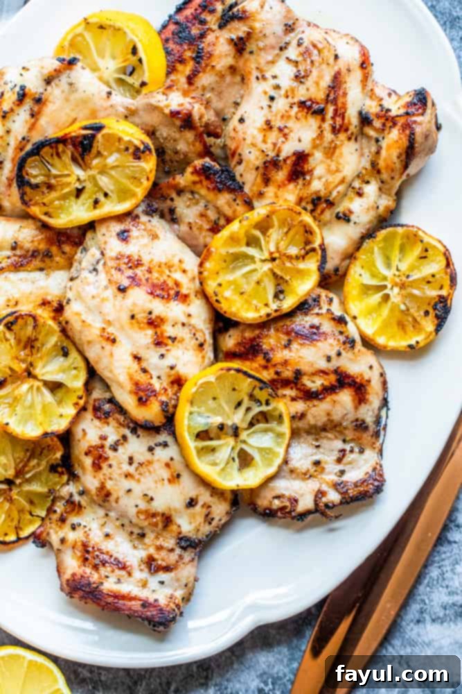 Overhead shot of perfectly grilled lemon pepper chicken thighs on a white plate, resting on a vibrant blue kitchen counter. The chicken is golden brown with visible char marks, and garnished with fresh lemon slices, highlighting its zesty flavor.
