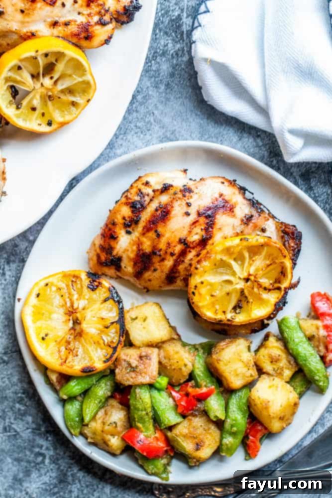 Grilled chicken thigh on a white plate on a blue counter, served with vibrant roasted vegetables on the side.