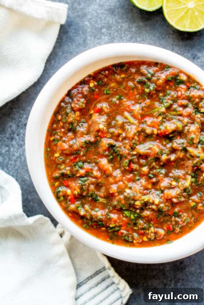 Easy Homemade Restaurant Style Salsa in a white bowl on a blue counter, ready to serve in minutes. Overhead shot of vibrant red restaurant style salsa in a white bowl, garnished with fresh cilantro, on a blue kitchen counter. Perfect for dipping tortilla chips.