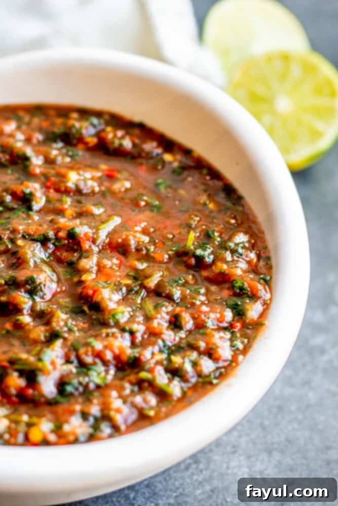 Close up shot of vibrant red restaurant style salsa in a white bowl, garnished with cilantro, sitting on a blue counter.