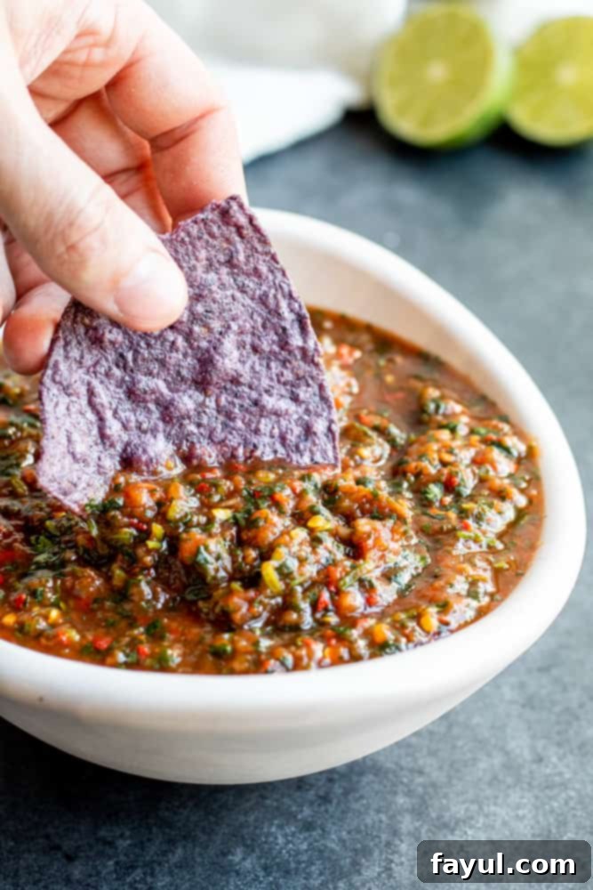 Hand dipping a blue corn tortilla chip into a white bowl of homemade restaurant style salsa on a blue counter.