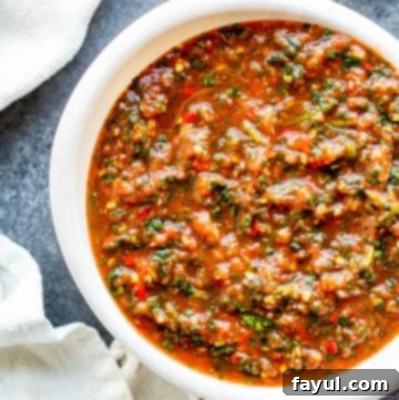 Overhead shot of vibrant red restaurant style salsa in a white bowl, garnished with fresh cilantro, on a blue kitchen counter.