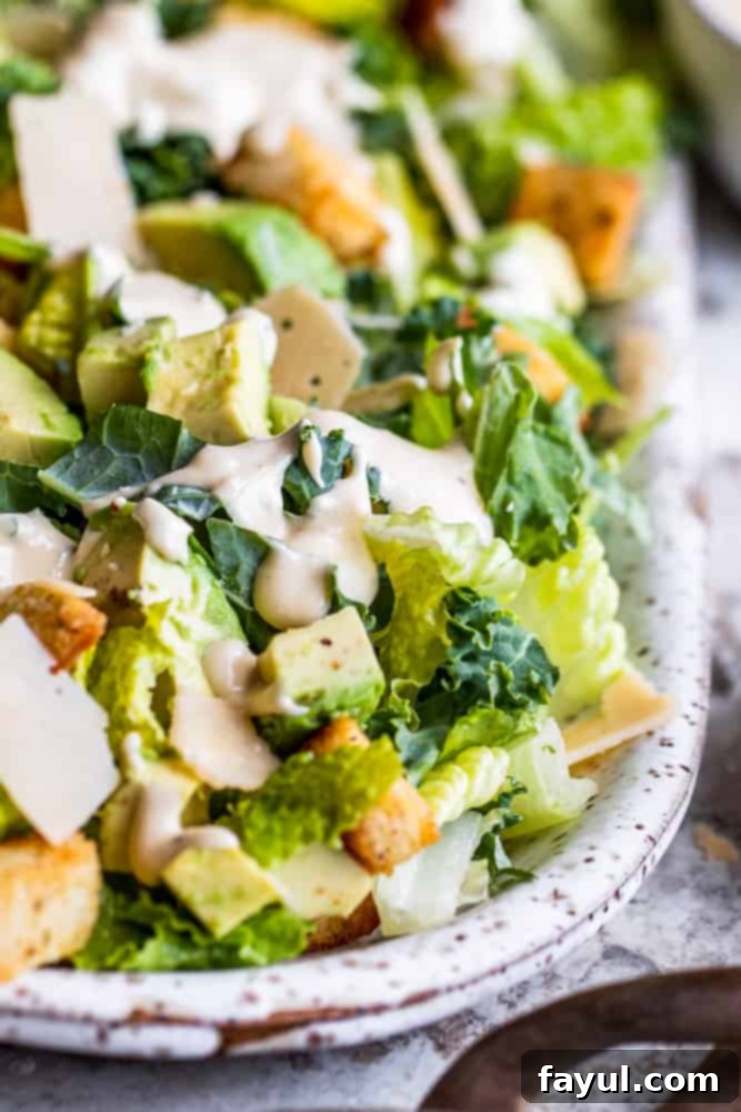 Healthy Kale Caesar Salad with creamy avocado, homemade croutons, and Parmesan cheese. Freshly prepared Kale Caesar Salad with creamy avocado, homemade croutons, and freshly grated Parmesan cheese on a white platter, ready to be served.