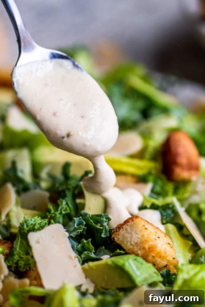 Drizzling Caesar dressing over fresh Kale Caesar Salad for ultimate flavor. Silver spoon elegantly drizzling creamy Caesar dressing over a beautifully assembled Kale Caesar Salad, ready to be tossed and served.