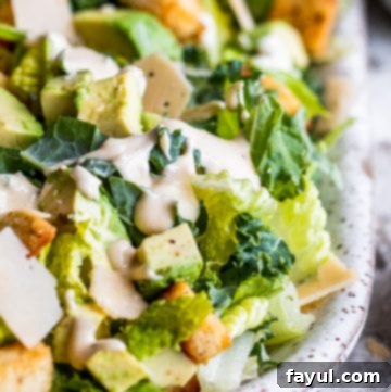 Close-up of a serving of Kale Caesar Salad with avocado on a white plate, highlighting its fresh ingredients and inviting texture.