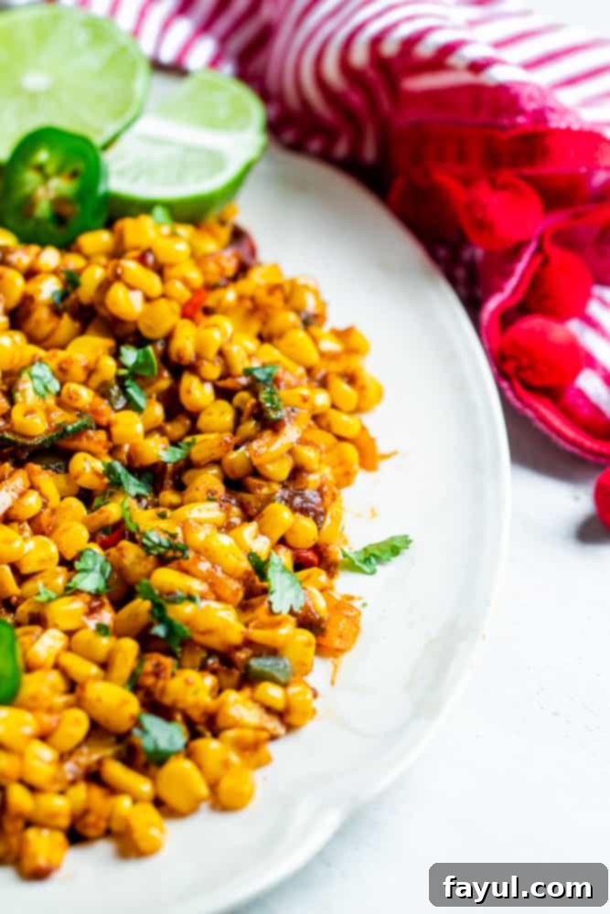 This Warm Mexican Corn Salad recipe is ready quickly in under 30 minutes and simple to make. This warm salad recipe features frozen corn, bell peppers, jalapeno, and zucchini. This corn and pepper salad is versatile and can be served on its own as a side dish or added to tacos, burritos, nachos or in a quesadilla. Warm Mexican corn salad served on a white oval platter, garnished with cilantro, placed on a white kitchen counter.