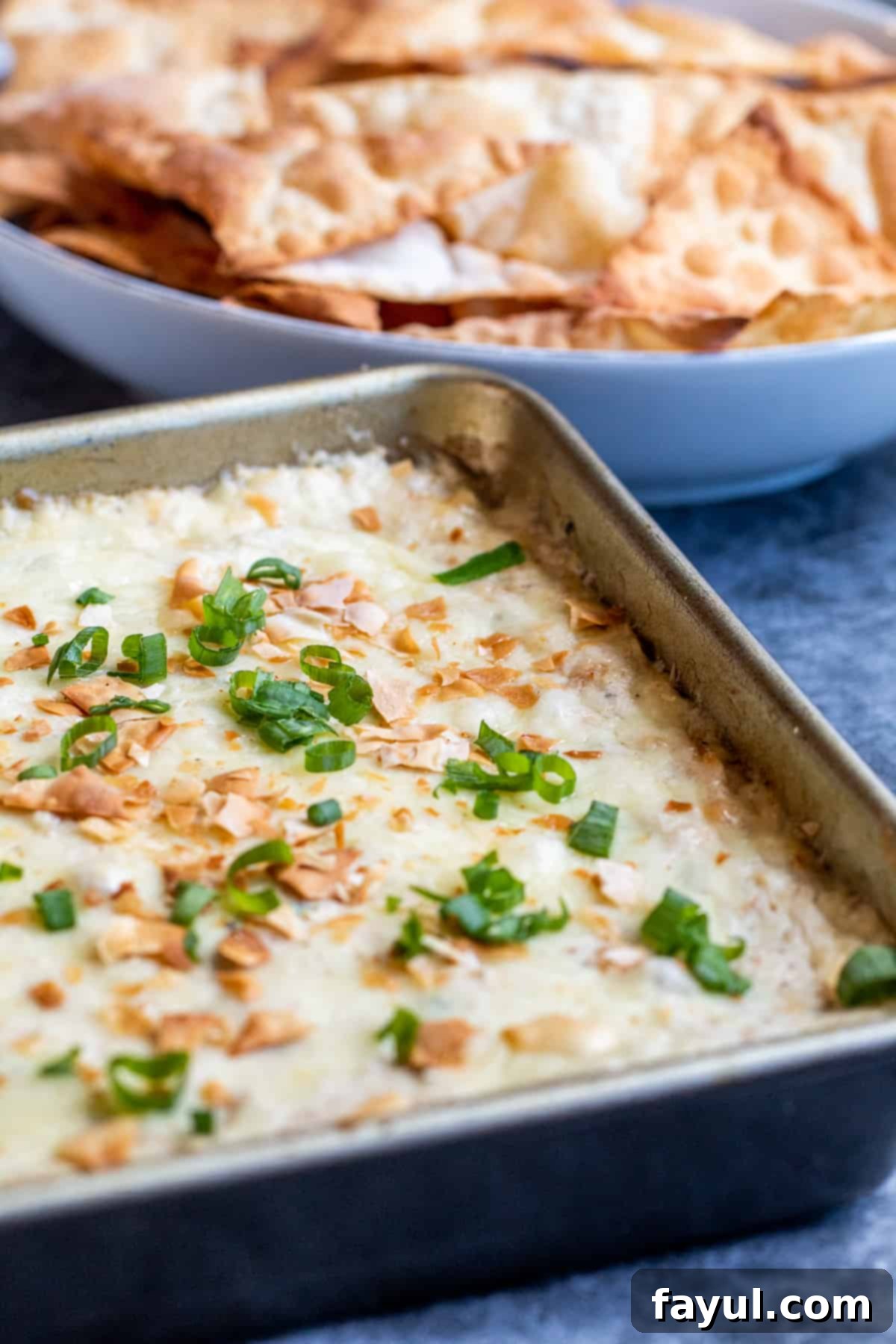 Creamy Crab Rangoon Dip with Crispy Wonton Dippers 2 Crab dip in a baking pan on a blue counter with chips in the background.