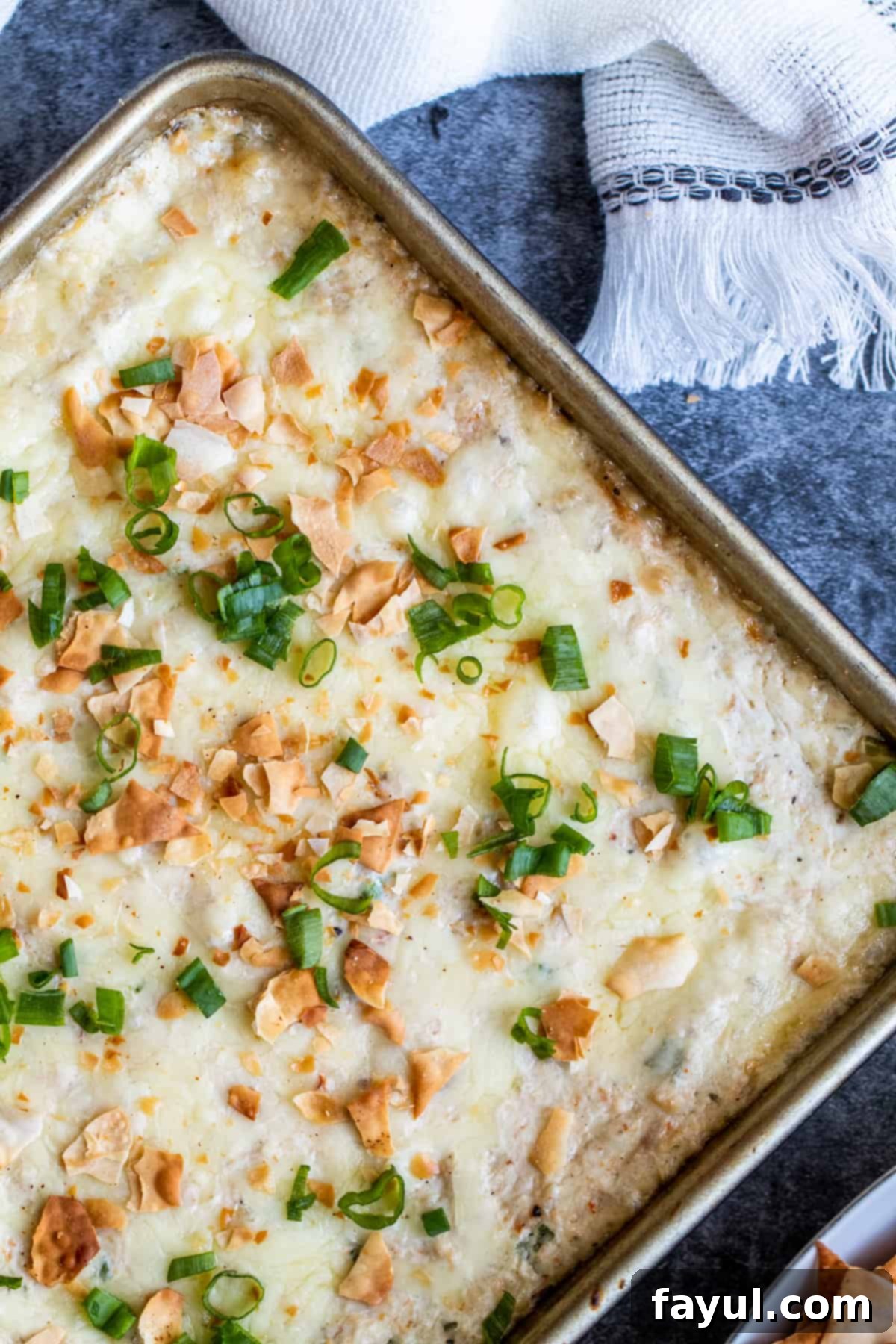 Creamy Crab Rangoon Dip with Crispy Wonton Dippers 5 Overhead shot of hot crab dip in a baking pan on a blue counter with white cloth.