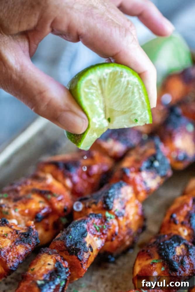 Chipotle Honey Glazed Chicken Skewers 5 Hand holding lime slice and squeezing juice over grilled chicken.