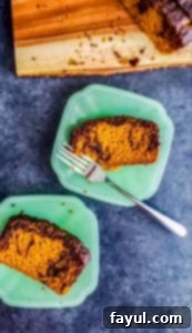 The BEST Pumpkin Spice Loaf Cake with Dark Chocolate Swirl recipe! This Pumpkin Bread recipe is super easy, and uses canned pumpkin. The bread is moist and you will love this homemade Fall recipe! #pumpkin #pumpkinbread #loafcake #Fall Two pieces of pumpkin spice loaf cake on teal plates on a gray counter top, with a prominent chocolate swirl.