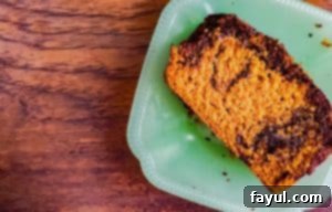 The BEST Pumpkin Spice Loaf Cake with Dark Chocolate Swirl recipe! This Pumpkin Bread recipe is super easy, and uses canned pumpkin. The bread is moist and you will love this homemade Fall recipe! #pumpkin #pumpkinbread #loafcake #Fall A close up shot of a slice of pumpkin bread on a glass teal plate, showing the beautiful moist crumb and chocolate swirl.