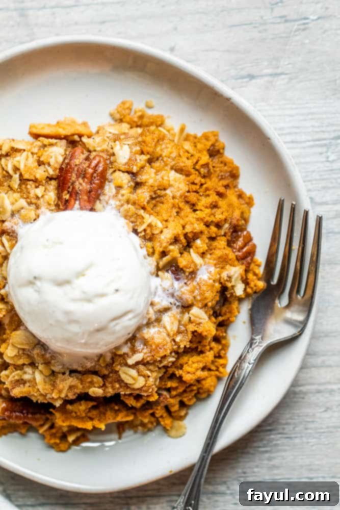 Irresistible Pumpkin Crisp featuring Pecan Oat Streusel 5 An overhead shot of a freshly baked pumpkin crisp on a white plate, ready to be served. A silver spoon is placed alongside the crisp, suggesting it's about to be enjoyed.