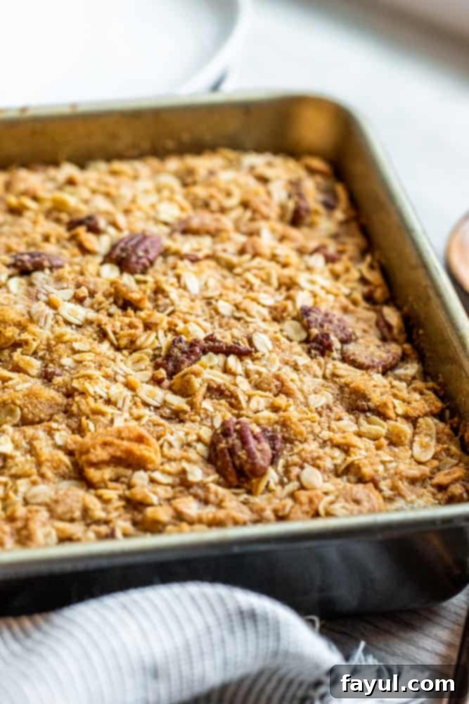 Irresistible Pumpkin Crisp featuring Pecan Oat Streusel 6 A freshly baked pumpkin crisp in a square white baking dish, presented on a minimalist white table. The topping is golden and bubbly, indicating it's just out of the oven and perfectly cooked.