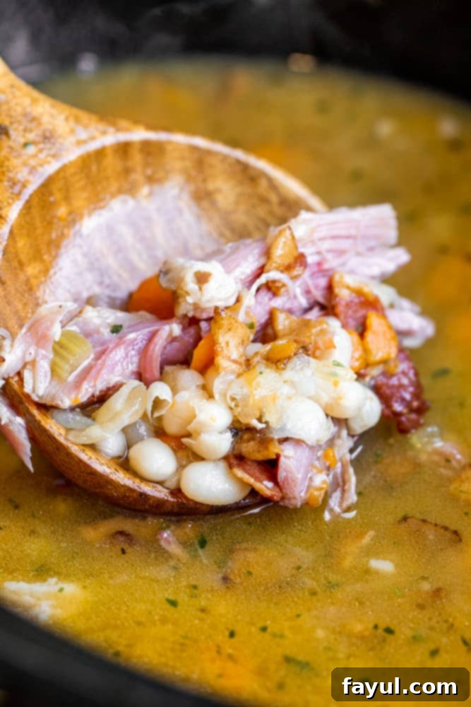 Slow-Cooked Southern Ham and Bean Soup 3 Wooden spoon scooping up a spoonful of rich, hearty ham and bean soup from a white bowl.