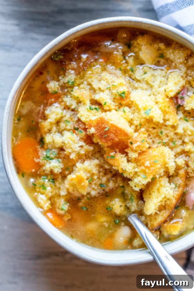 Slow-Cooked Southern Ham and Bean Soup 7 Overhead shot of a white bowl of ham and bean soup with a silver spoon inside, garnished with fresh parsley.