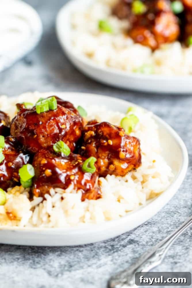 Fiery Asian Pork Meatballs 5 Two white plates of rice with meatballs on top.