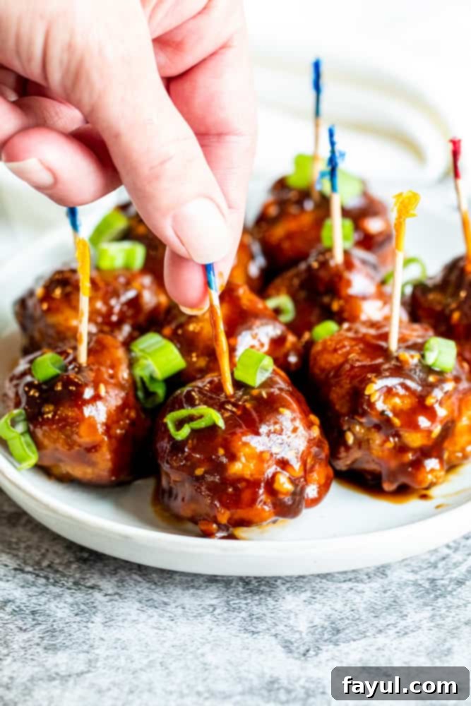 Fiery Asian Pork Meatballs 6 Hand picking up sticky meatball by toothpick.