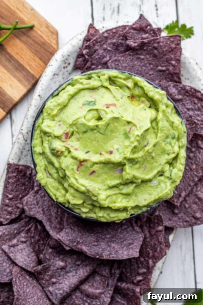 Overhead shot of a bowl of creamy guacamole with blue corn tortilla chips on a white counter, emphasizing freshness and vibrant color.