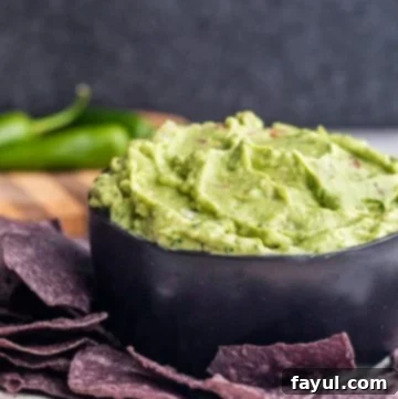Angle shot of incredibly creamy guacamole in a sleek black bowl, garnished with fresh cilantro and ready for dipping with chips.