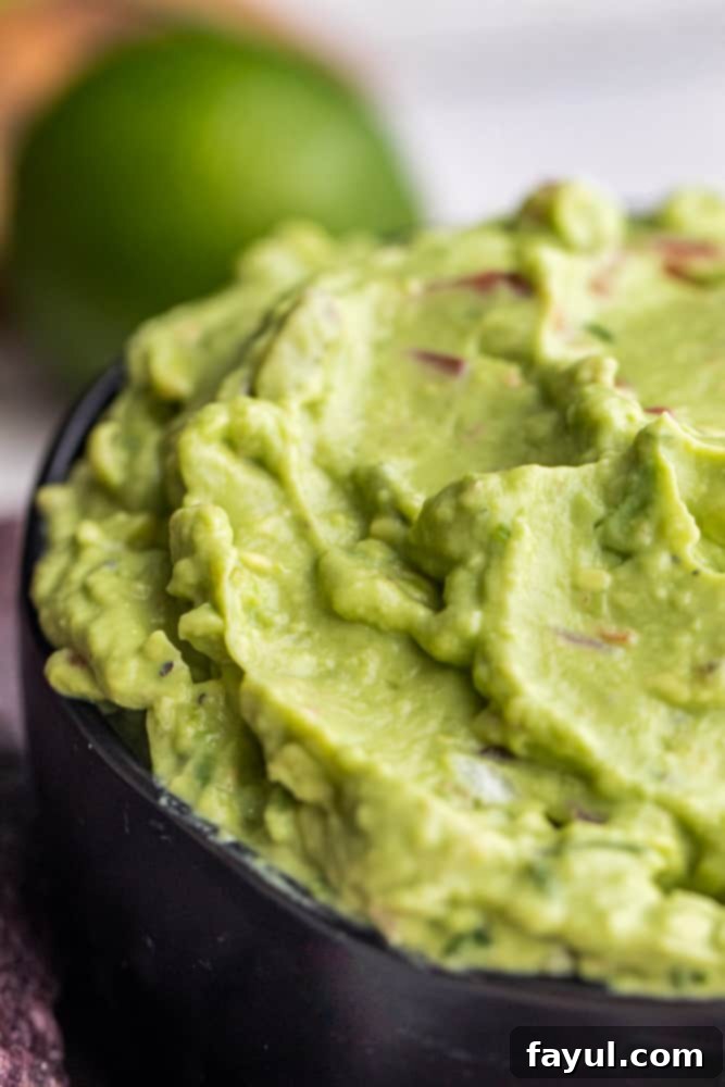 Close up image of creamy guacamole dip in a black bowl, highlighting its smooth texture and vibrant color.