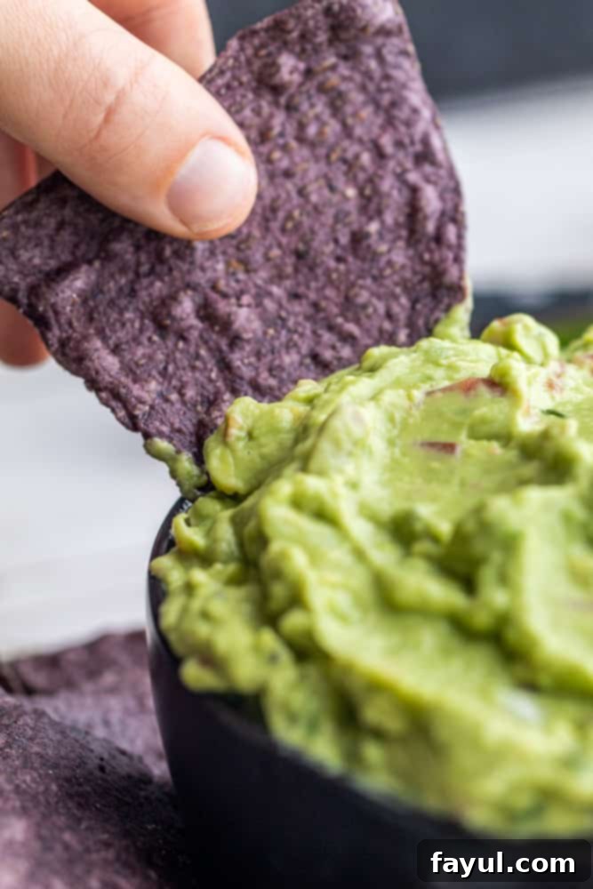A hand dipping a vibrant blue tortilla chip into a bowl of creamy avocado dip, highlighting the texture and appeal.
