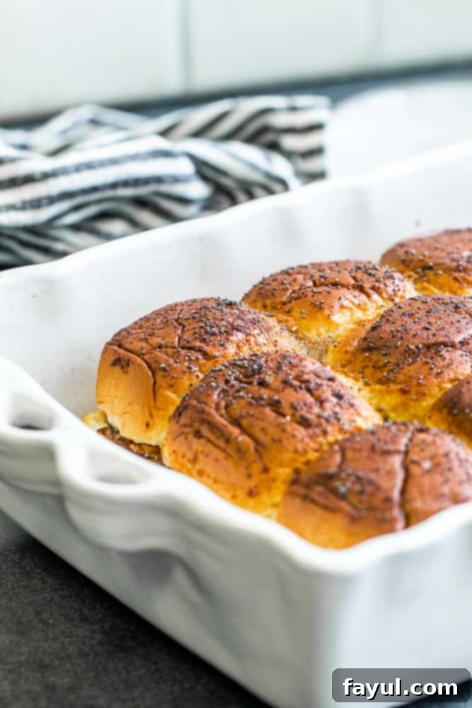 Effortless Baked Roast Beef Sliders 2 Sliders in a white pan on a dark countertop.