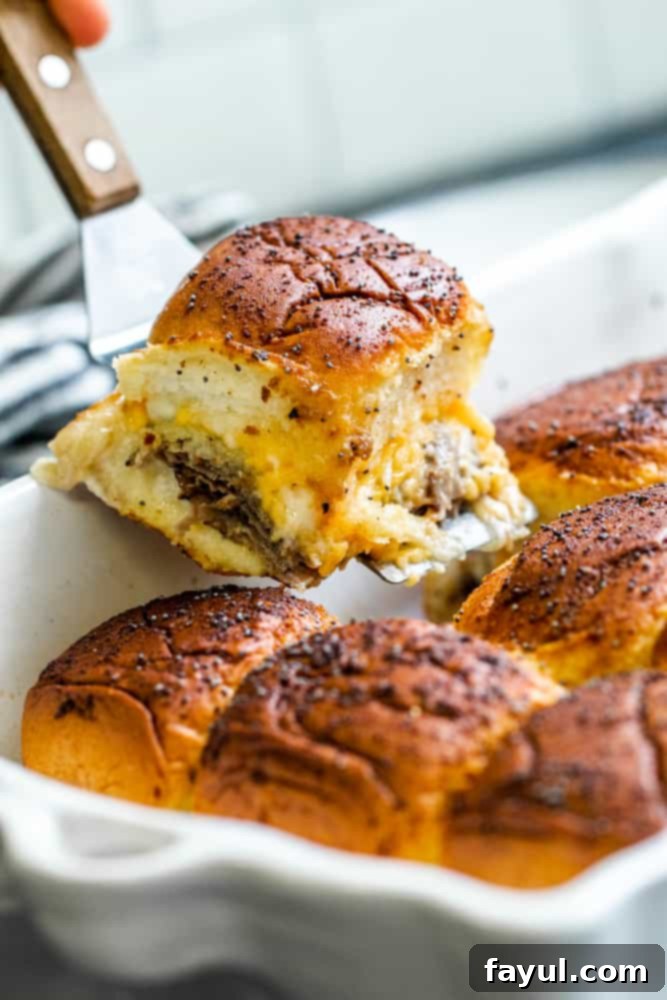 Effortless Baked Roast Beef Sliders 5 Spatula picking up one slider out of white pan.
