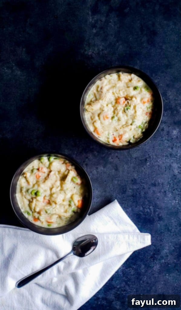 Hearty Slow Cooker Chicken and Dumplings with Fluffy Biscuits 5 Two black bowls filled with crockpot chicken and dumplings with biscuits. The bowls are on a dark blue surface. There is a white cloth with a silver spoon on the bottom part of the photo.