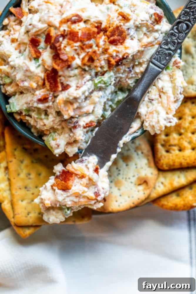 Close-up overhead shot of the creamy Million Dollar Dip in a blue bowl, highlighting its rich texture and the visible pieces of crispy bacon and crunchy almonds, with a silver serving knife resting on the edge.