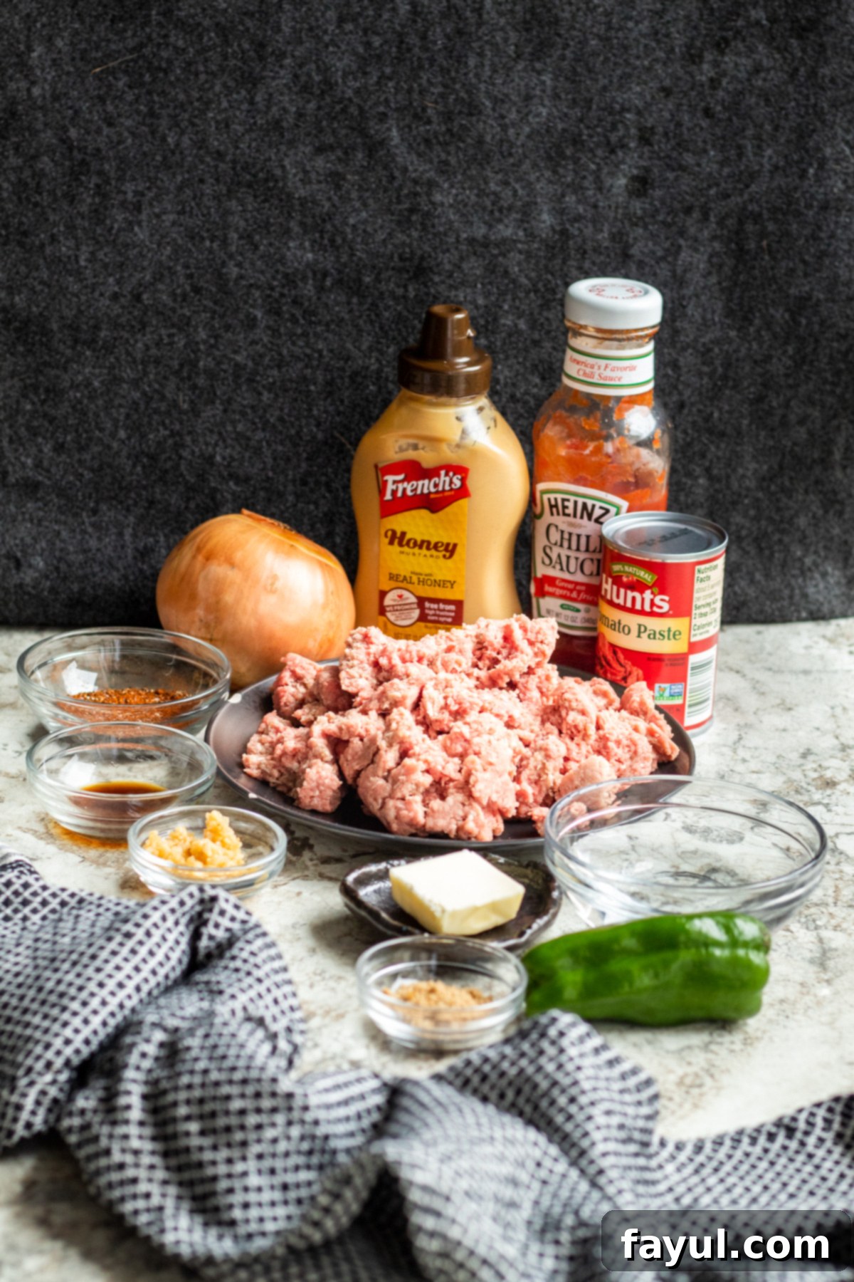 Sloppy joe ingredients on a white counter with gray background in jars and glass bowls.