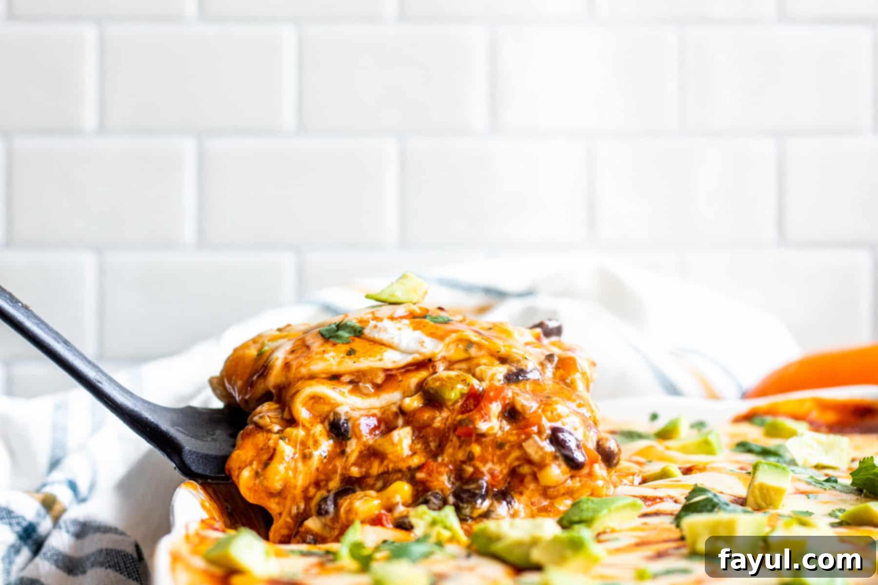 A serving of hot, cheesy vegetarian Mexican lasagna being scooped out of a white baking dish with a spatula.