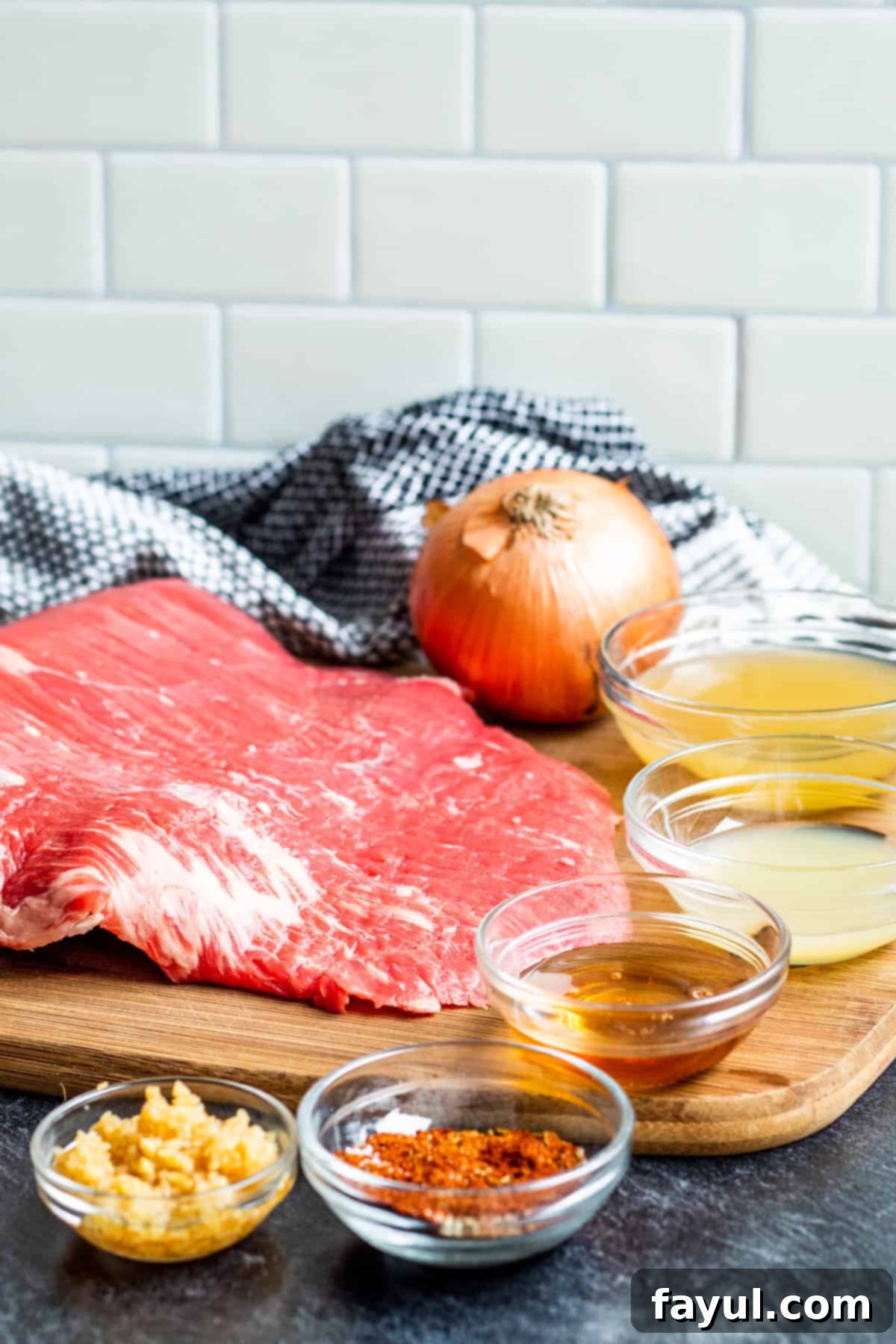 Ingredients for carne asada laid out on blue counter in glass cups, showing various spices and liquids.