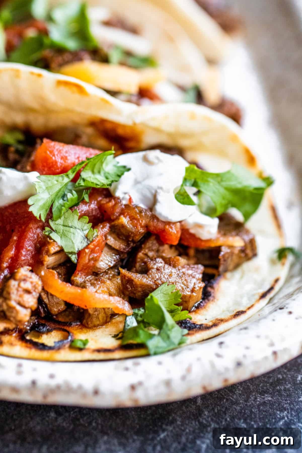 Angle shot of a line of three carne asada tacos on a white tray, garnished with cilantro.